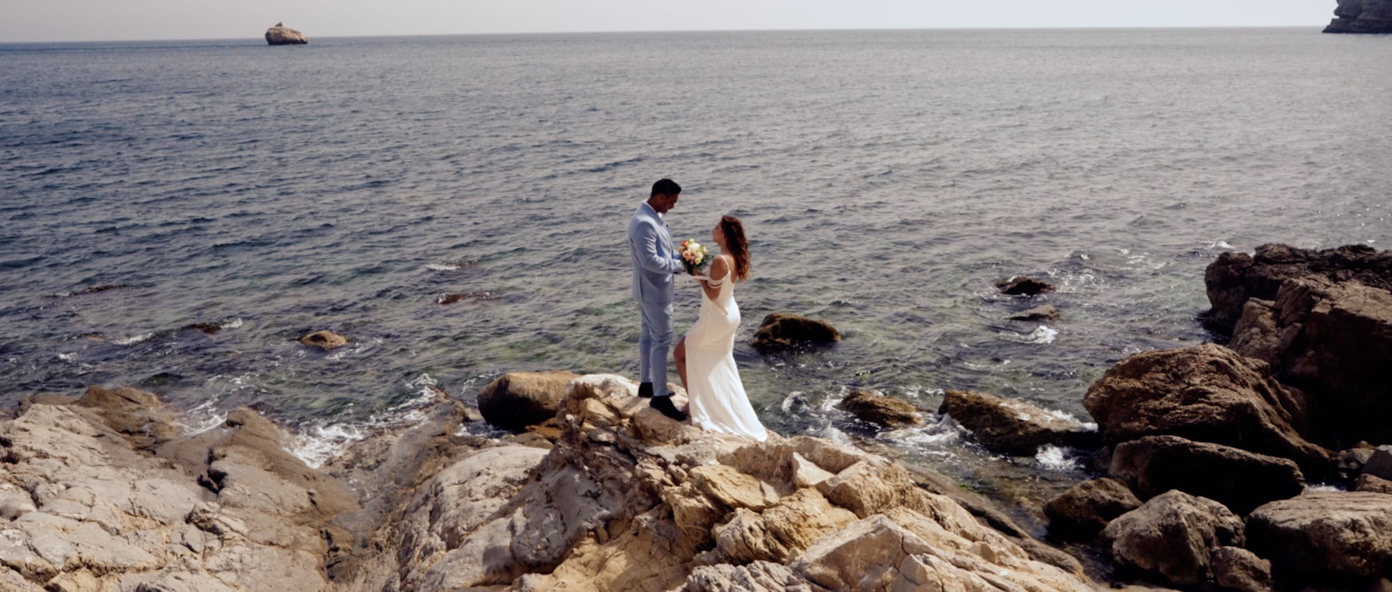 An intimate elopement captured by Stories by DJ — a couple exchanging vows on sun-kissed coastal rocks overlooking the Mediterranean Sea in Spain. A timeless moment filmed by an elopement videographer who specializes in romantic seaside escapes.